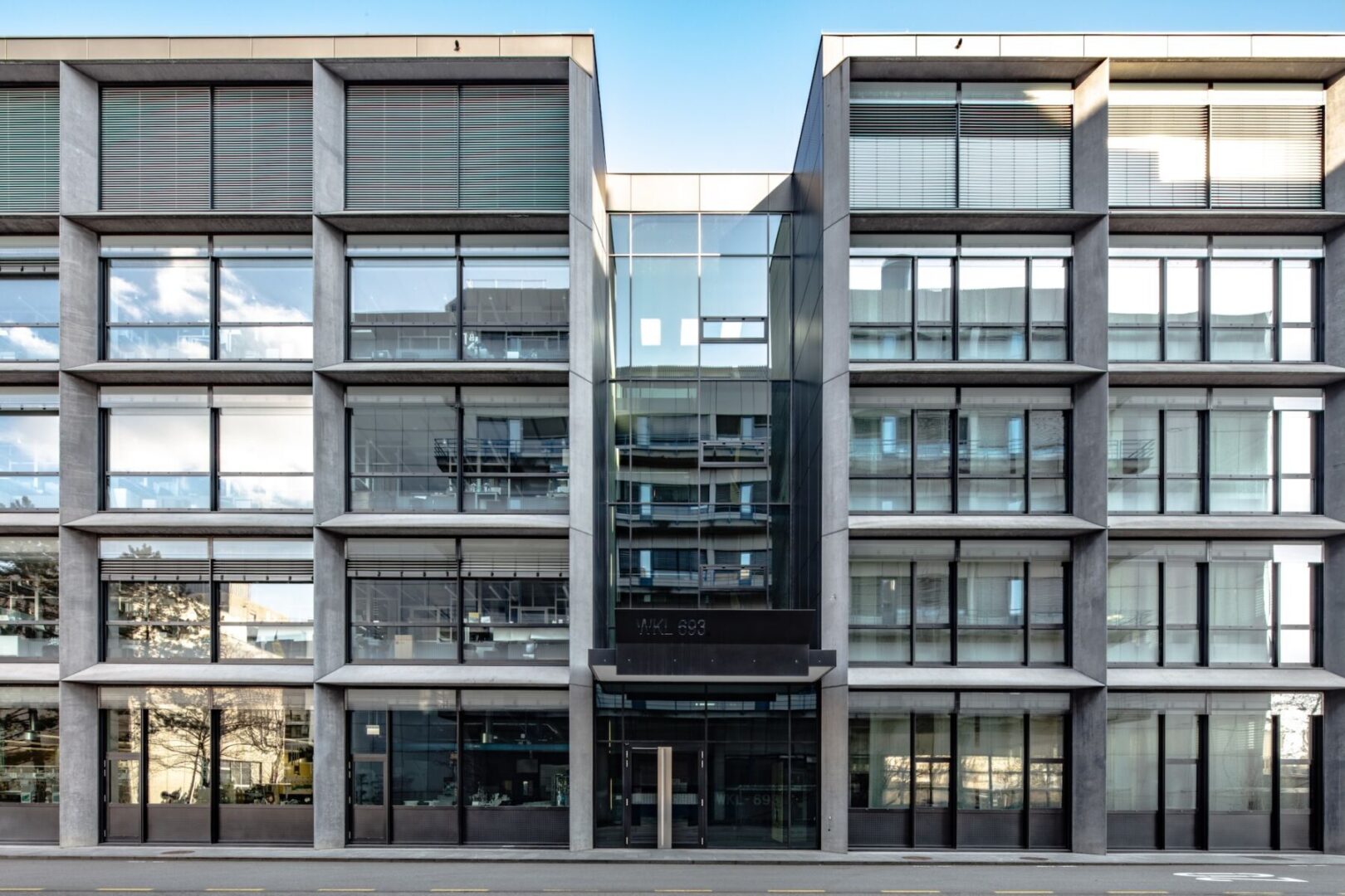 Modern office building with glass facade and concrete pillars under clear blue sky.