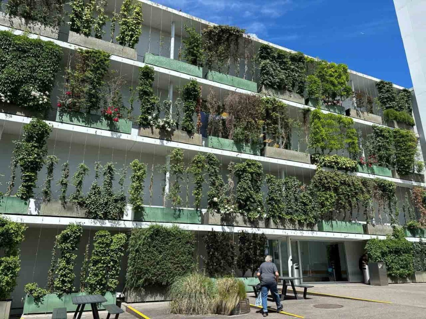 A modern building with lush vertical gardens and people walking nearby.