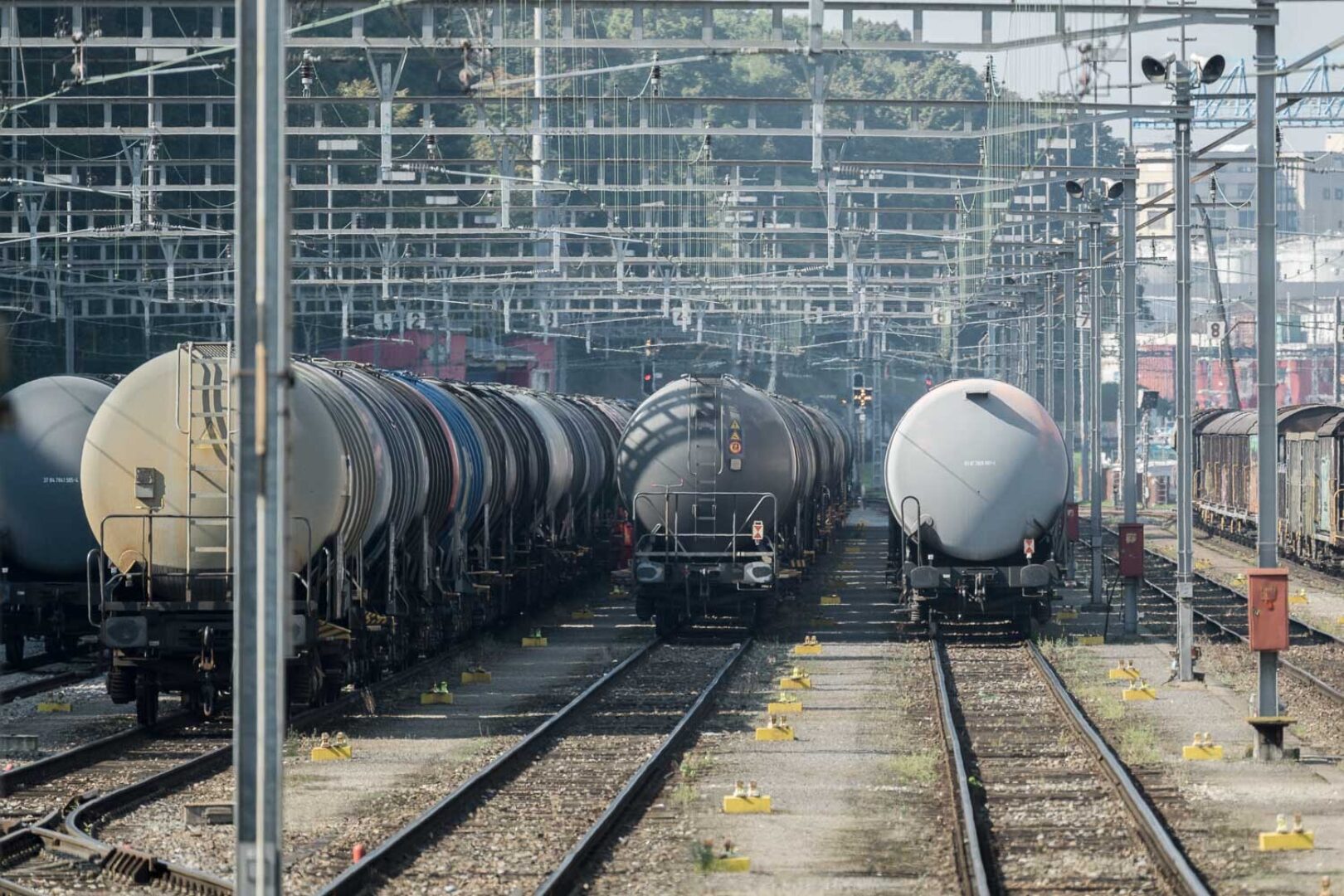 A train with multiple tanker cars travels along railway tracks in a station.