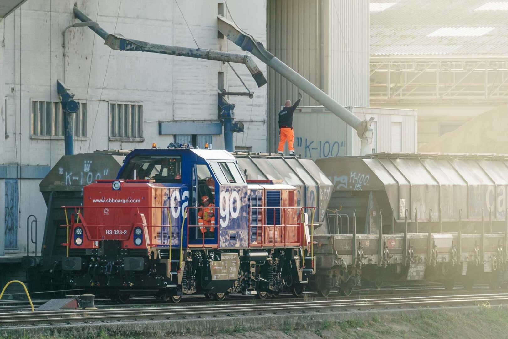 A red and blue train engine with the text "go" on it, pulling freight cars in a rail yard.