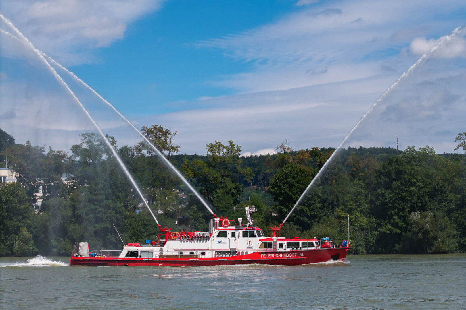 A red and white fireboat sprays water high into the air on a river.