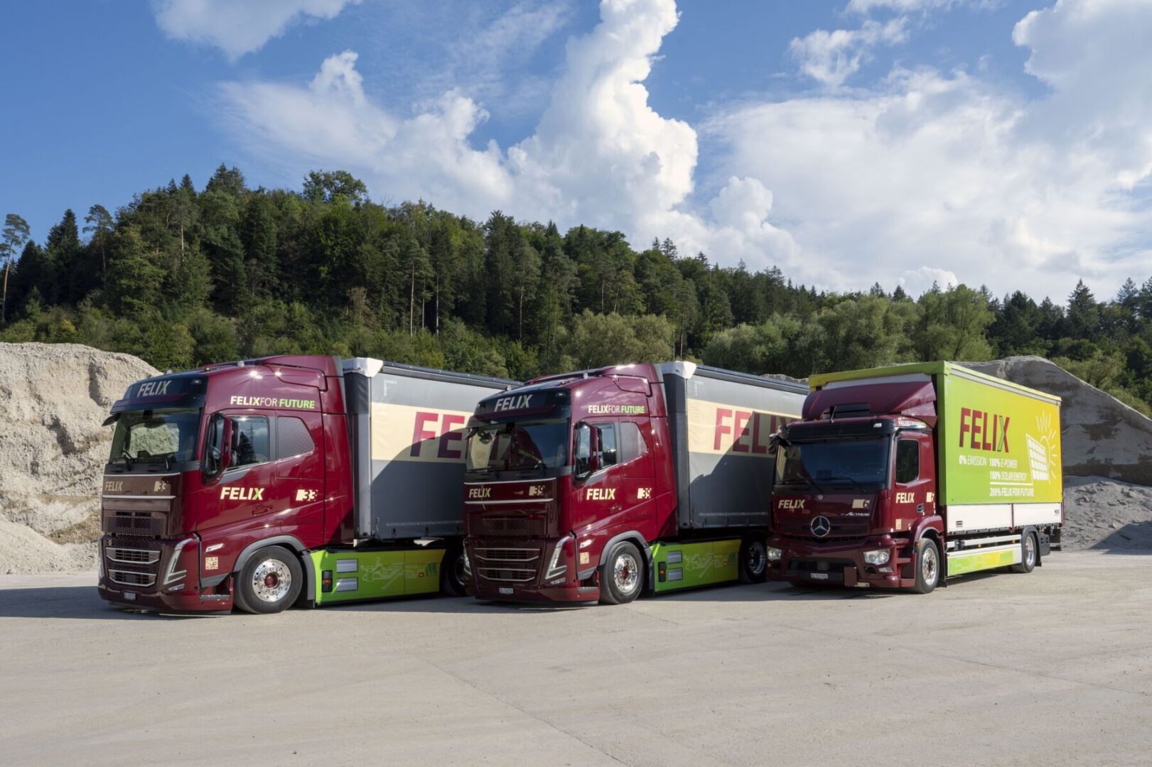 Three red Felix trucks parked side by side in a lot with a forested hill in the background.