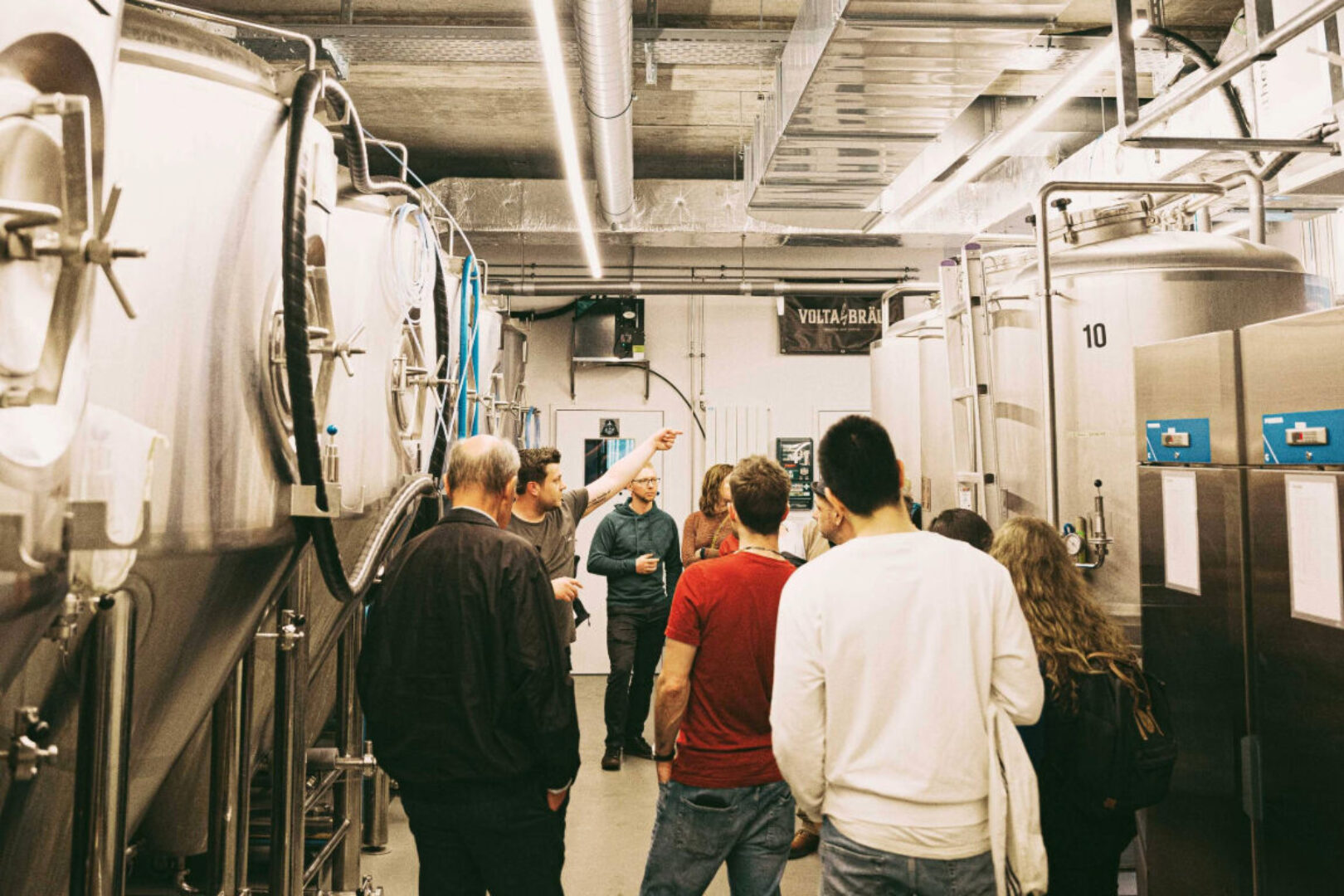 A group of people touring a brewery, observing large stainless steel brewing tanks.