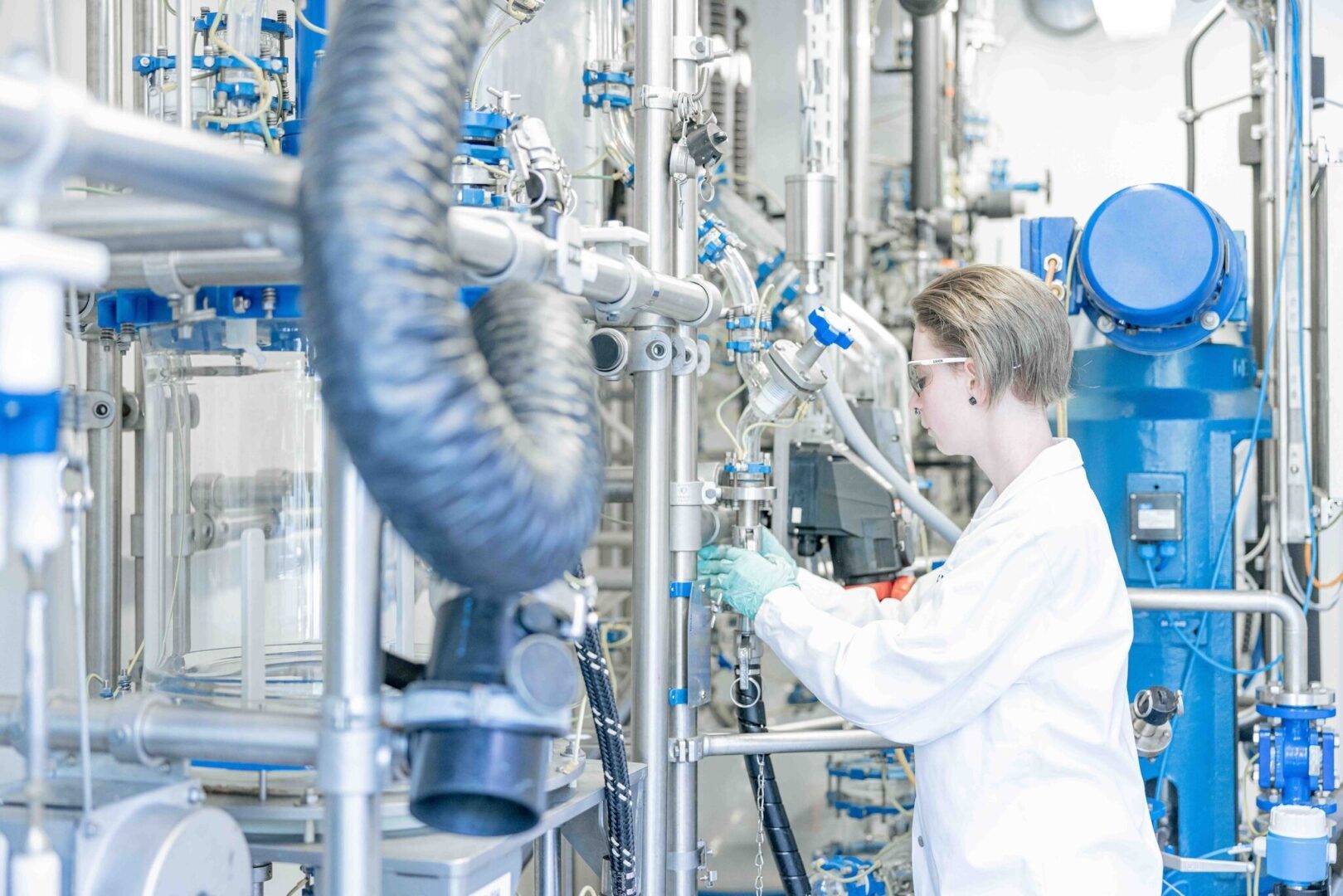 Wissenschaftlerin in weißem Kittel arbeitet in einem Labor mit komplexen Geräten.