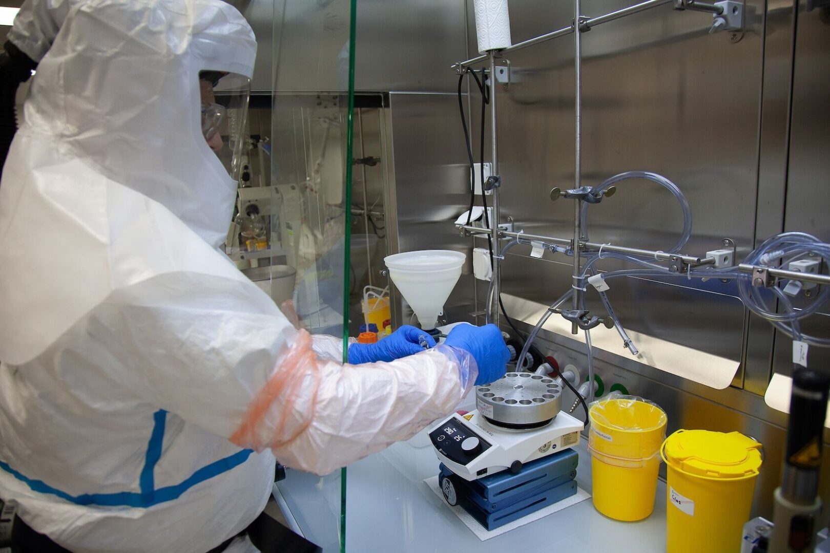 Eine Person in Schutzausrüstung arbeitet in einem Labor mit Zentrifugen und gelben Behältern.