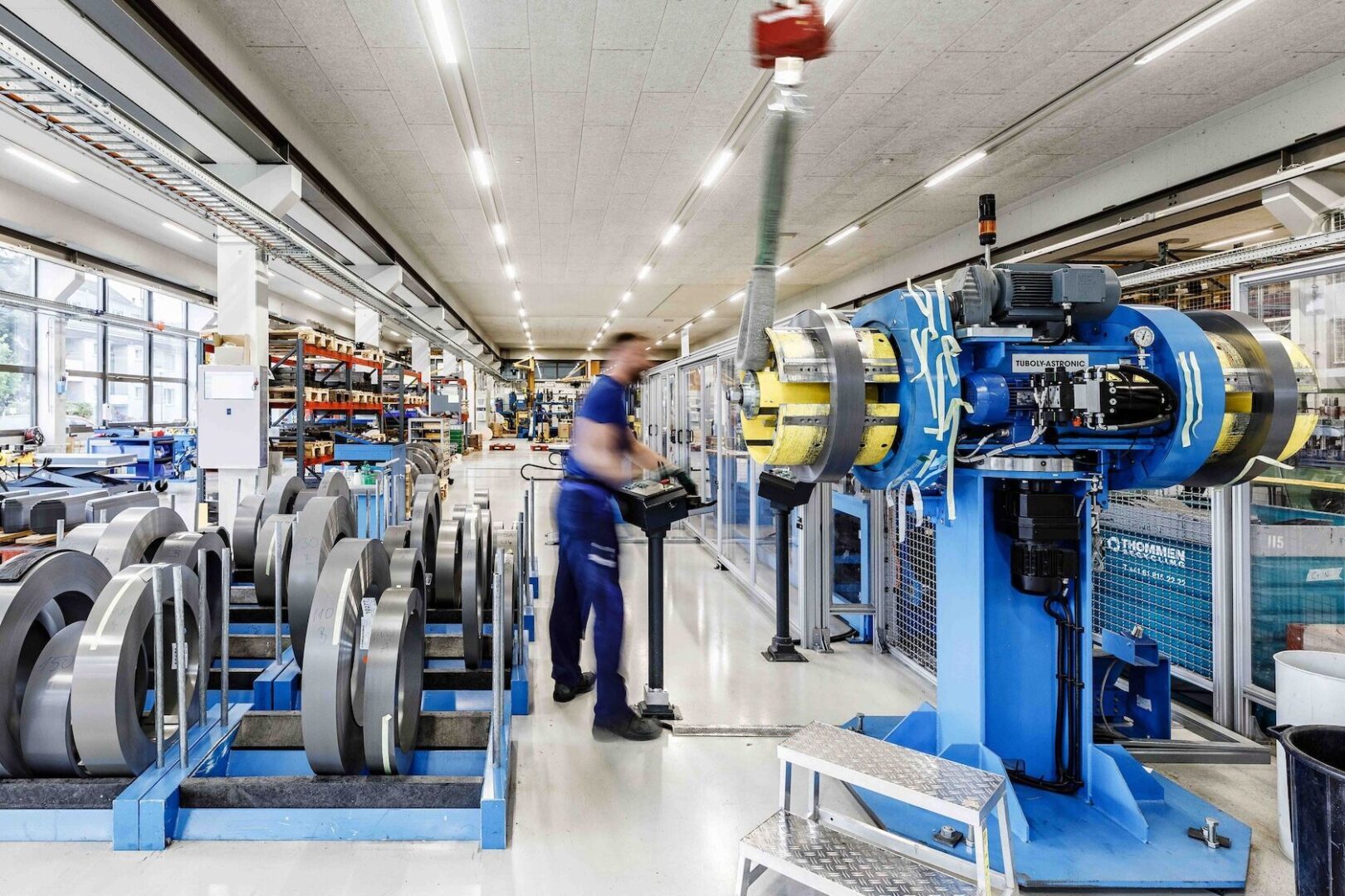 Arbeiter bedient eine große Maschine in einer Fabrik mit vielen Spulen.