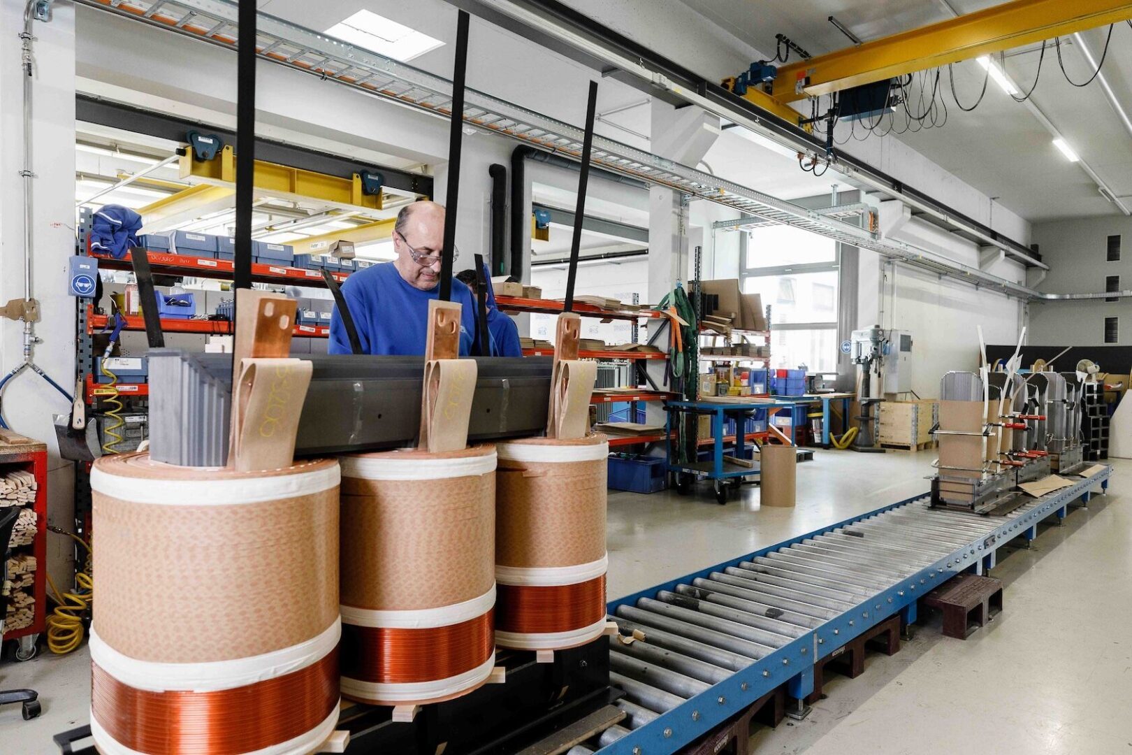 Mann in einer Fabrik mit großen Spulen aus Kupferdraht.
