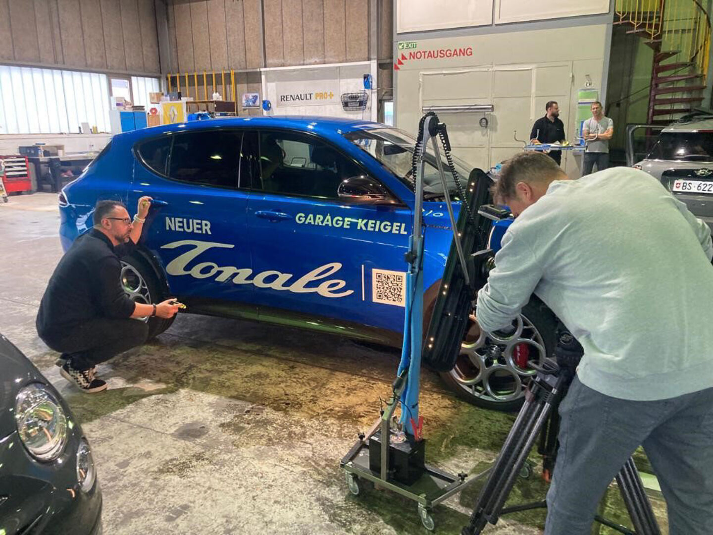 Keigel werkstatt Zwei Männer arbeiten an einem blauen Auto in einer Werkstatt.