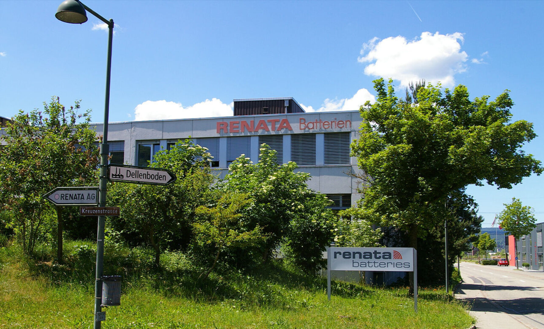 Gebäude mit RENATA Batterien Schriftzug und Straßenschildern vor grünem Hintergrund.