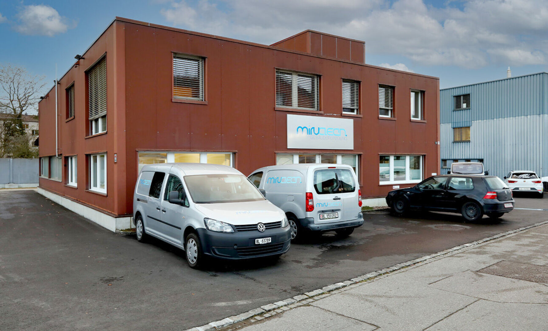 Ein braunes Gebäude mit drei parkenden Autos davor.