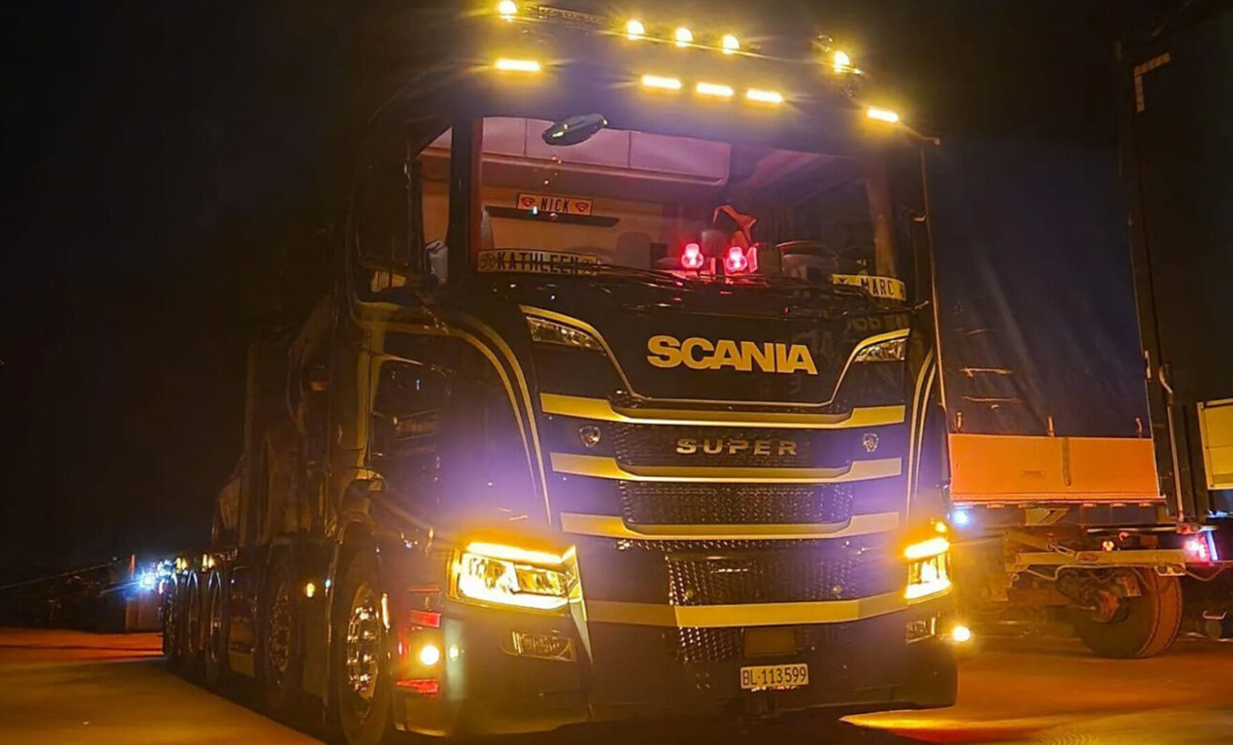 Ein LKW der Marke Scania fährt nachts auf einer Straße.