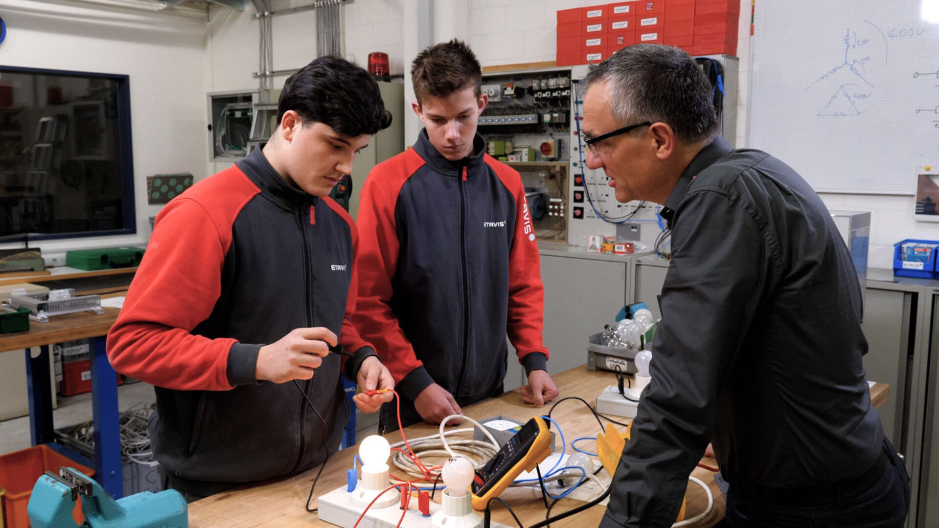 Three people are working together on an electrical experiment in a lab.