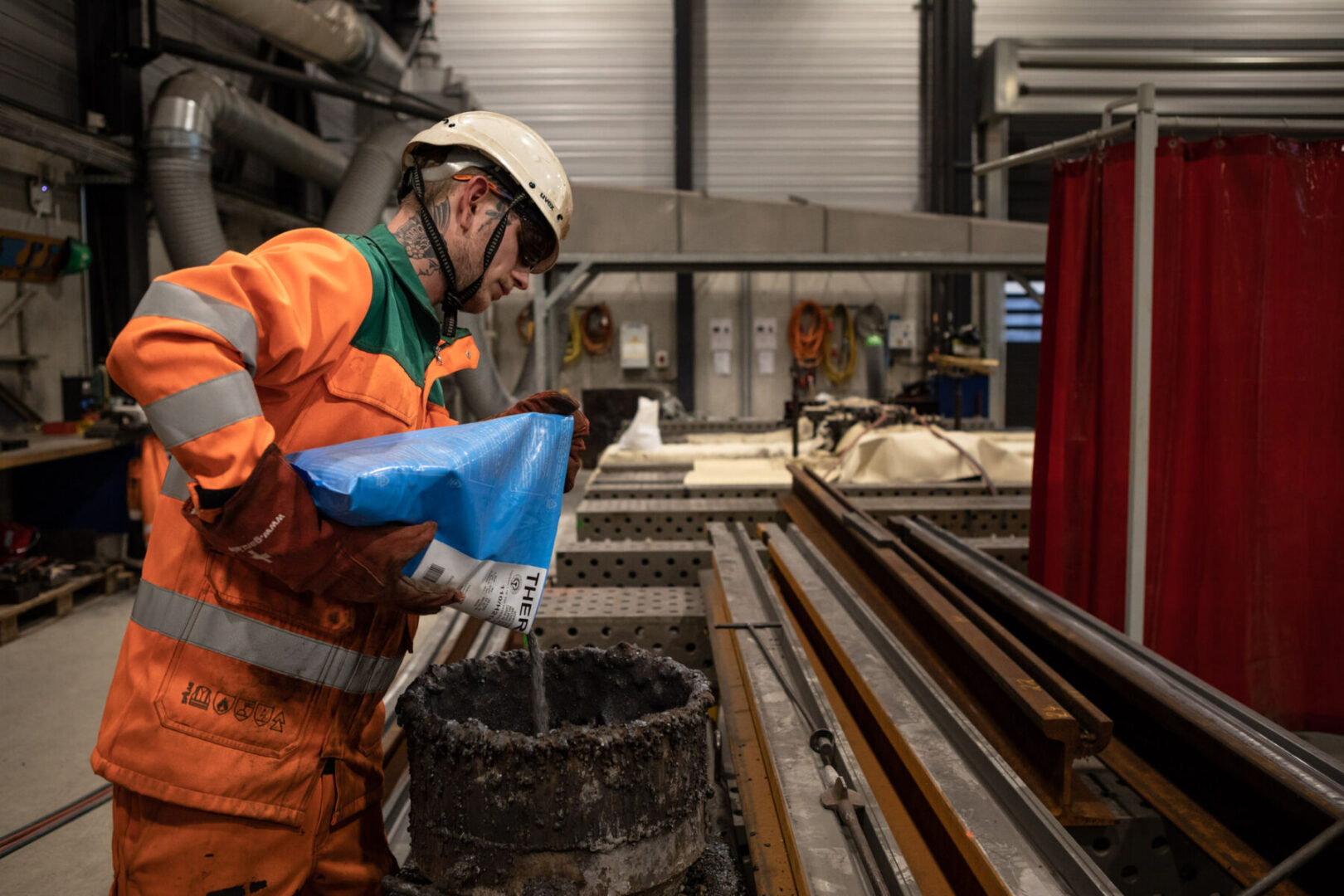 Ein Arbeiter in Schutzausrüstung gießt Material in eine Form in einer Fabrik.