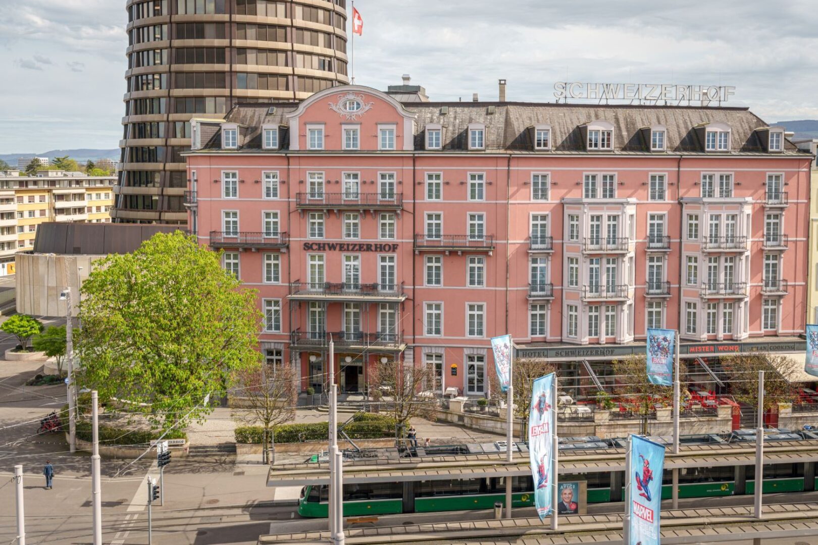 Pinkes Hotelgebäude mit dem Namen "Schweizerhof" und ein modernes Hochhaus daneben.
