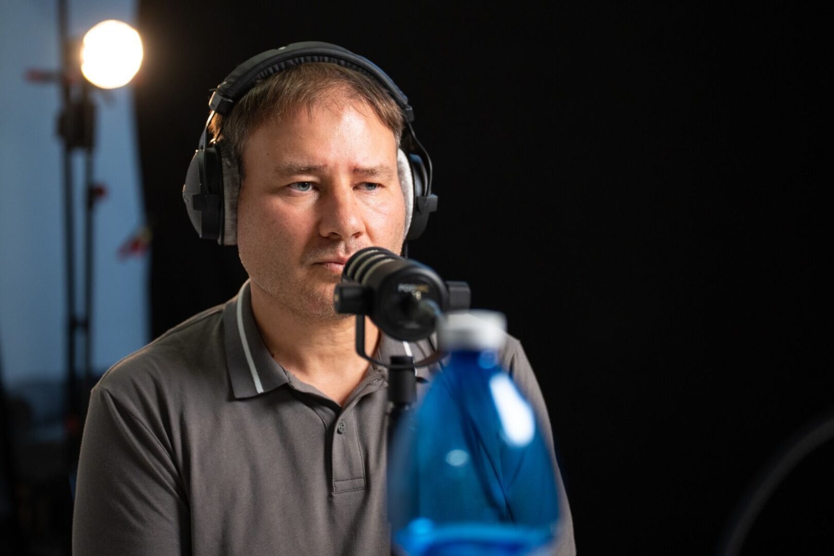 Ein Mann mit Kopfhörern sitzt konzentriert vor einem Mikrofon in einem Studio.