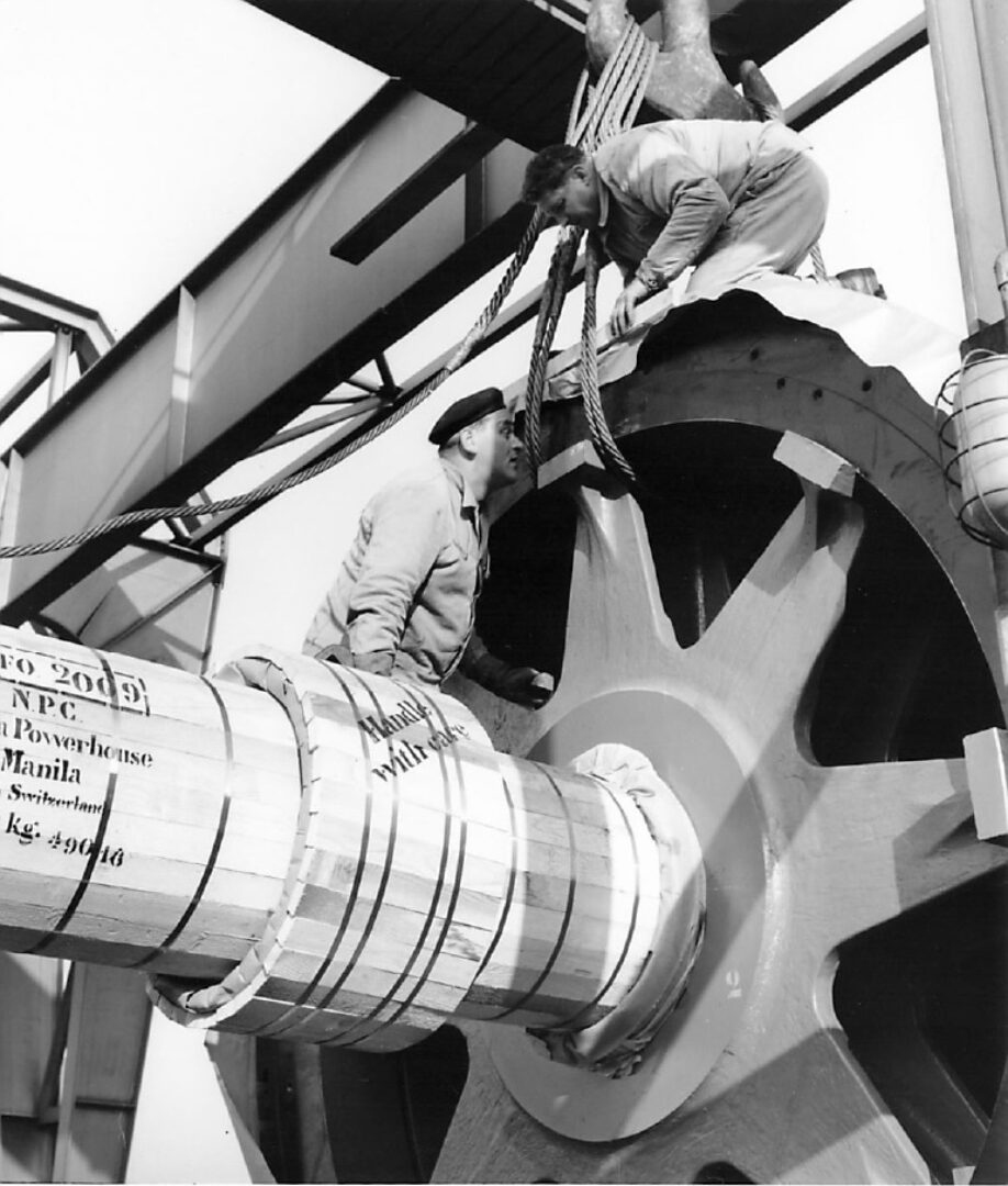 Zwei Männer heben ein großes Holzfass mit einem Flaschenzug.