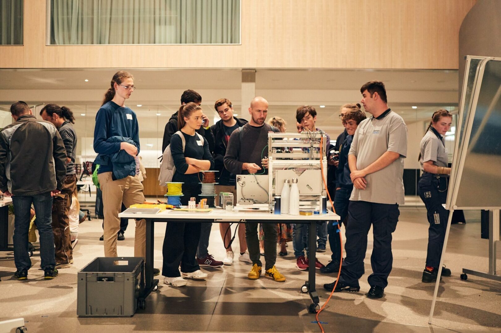 Eine Gruppe von Menschen steht um einen 3D-Drucker herum und beobachtet den Druckvorgang.