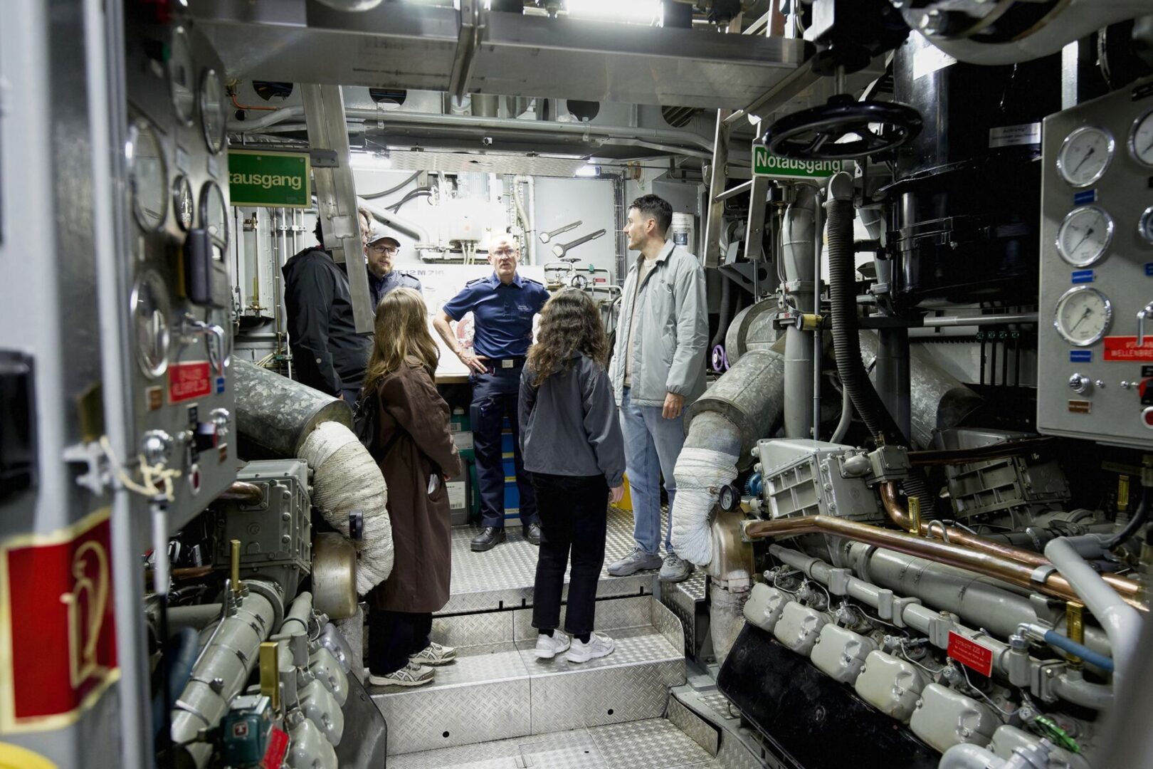 Eine Gruppe von Menschen besucht den Maschinenraum eines Schiffes.