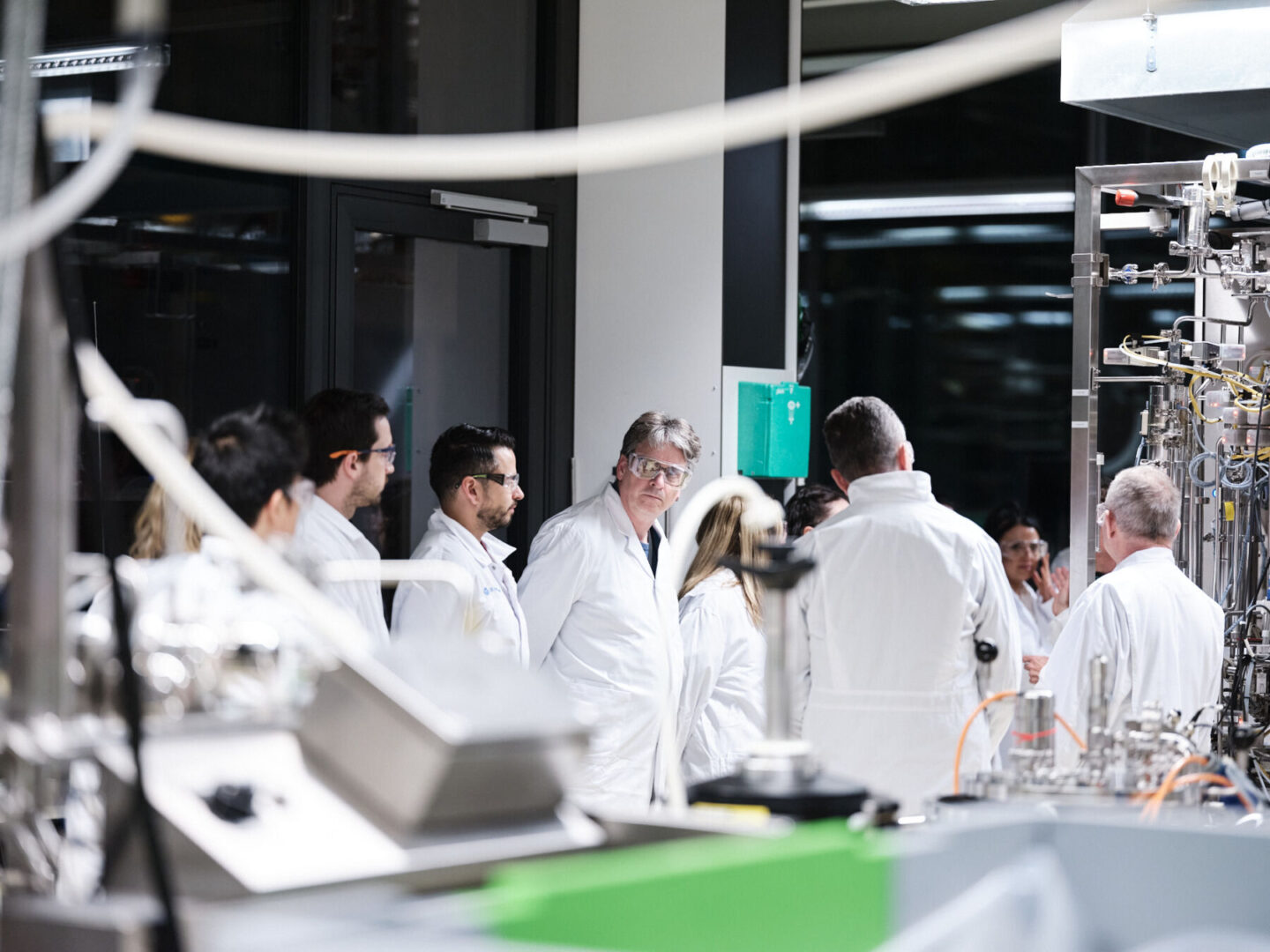 Wissenschaftler in Laborkitteln diskutieren vor Laborausrüstung.