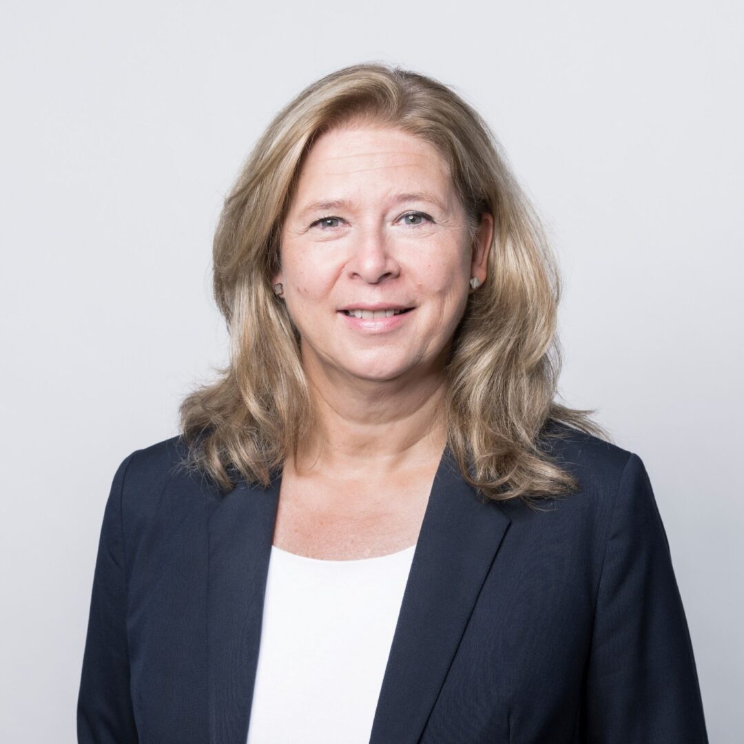 Porträt einer lächelnden Frau mit blonden Haaren in einem dunklen Blazer.