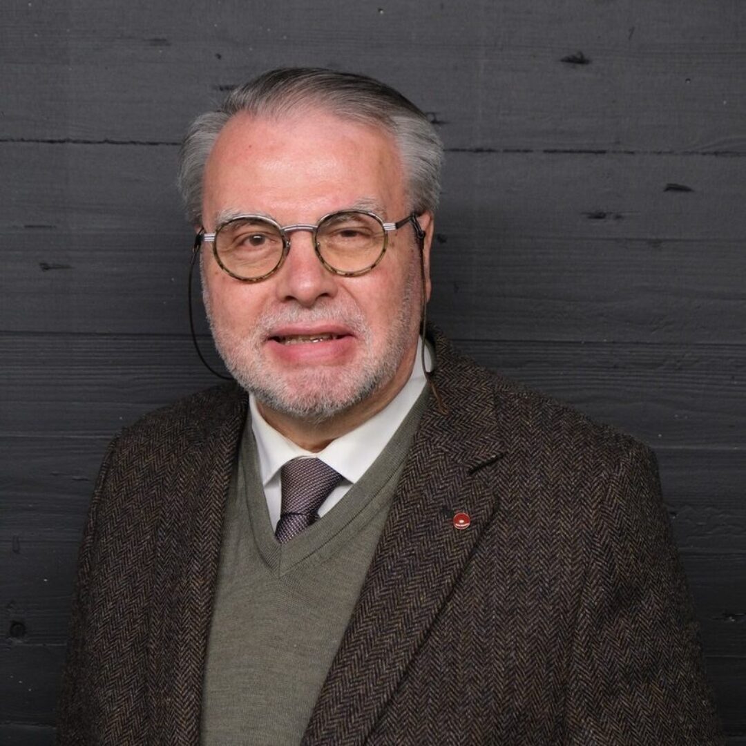 Ein älterer Mann mit Brille und Anzug lächelt in die Kamera.