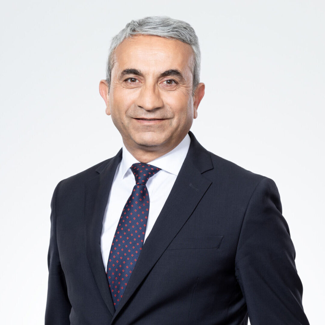 Ein lächelnder Mann mit grauem Haar im Anzug und Krawatte.