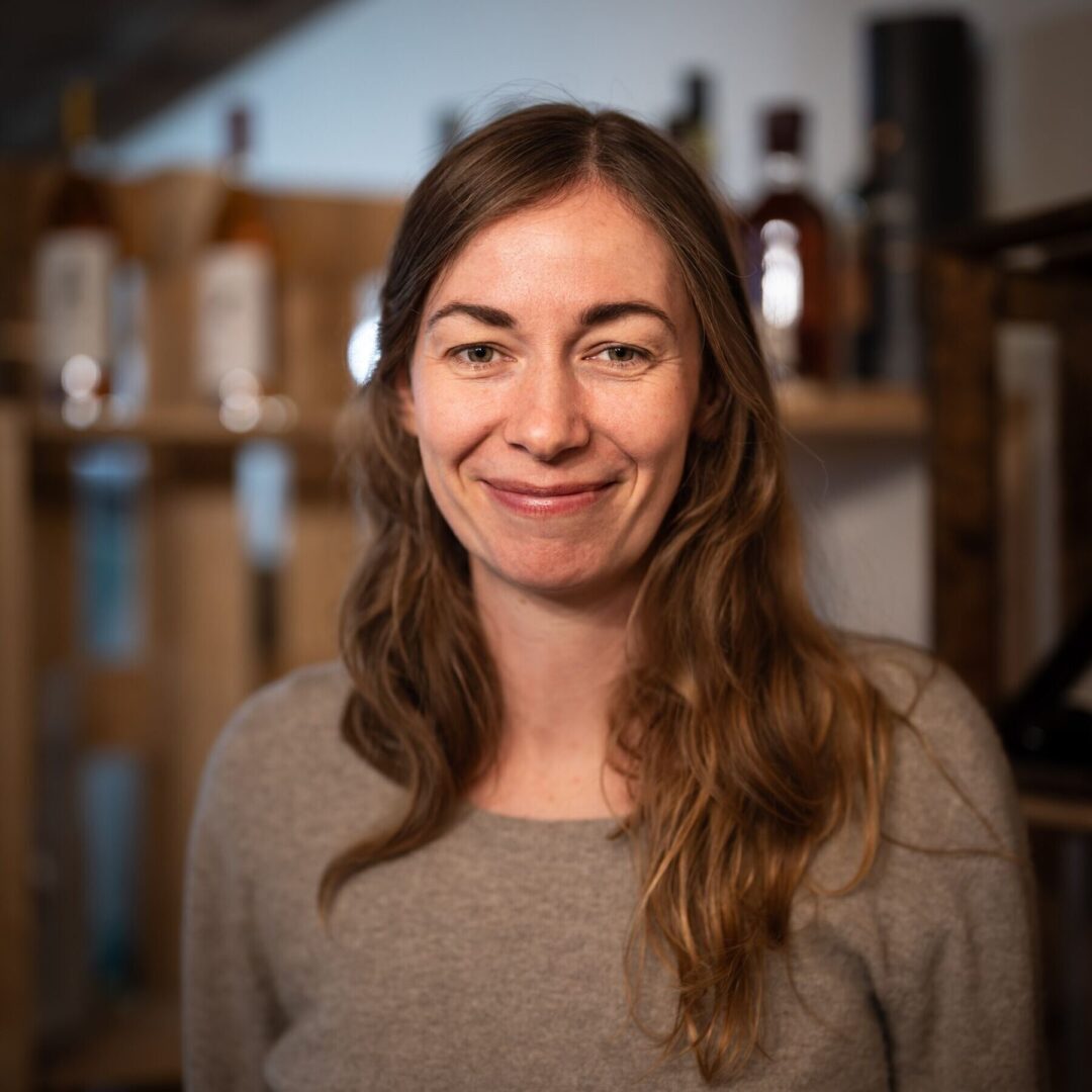 Eine lächelnde Frau mit langen Haaren in einem Raum mit Holzvertäfelung.